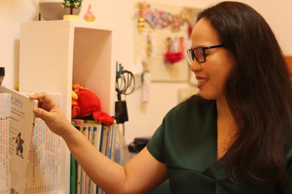 Teacher Jan beside a bookshelf at her place