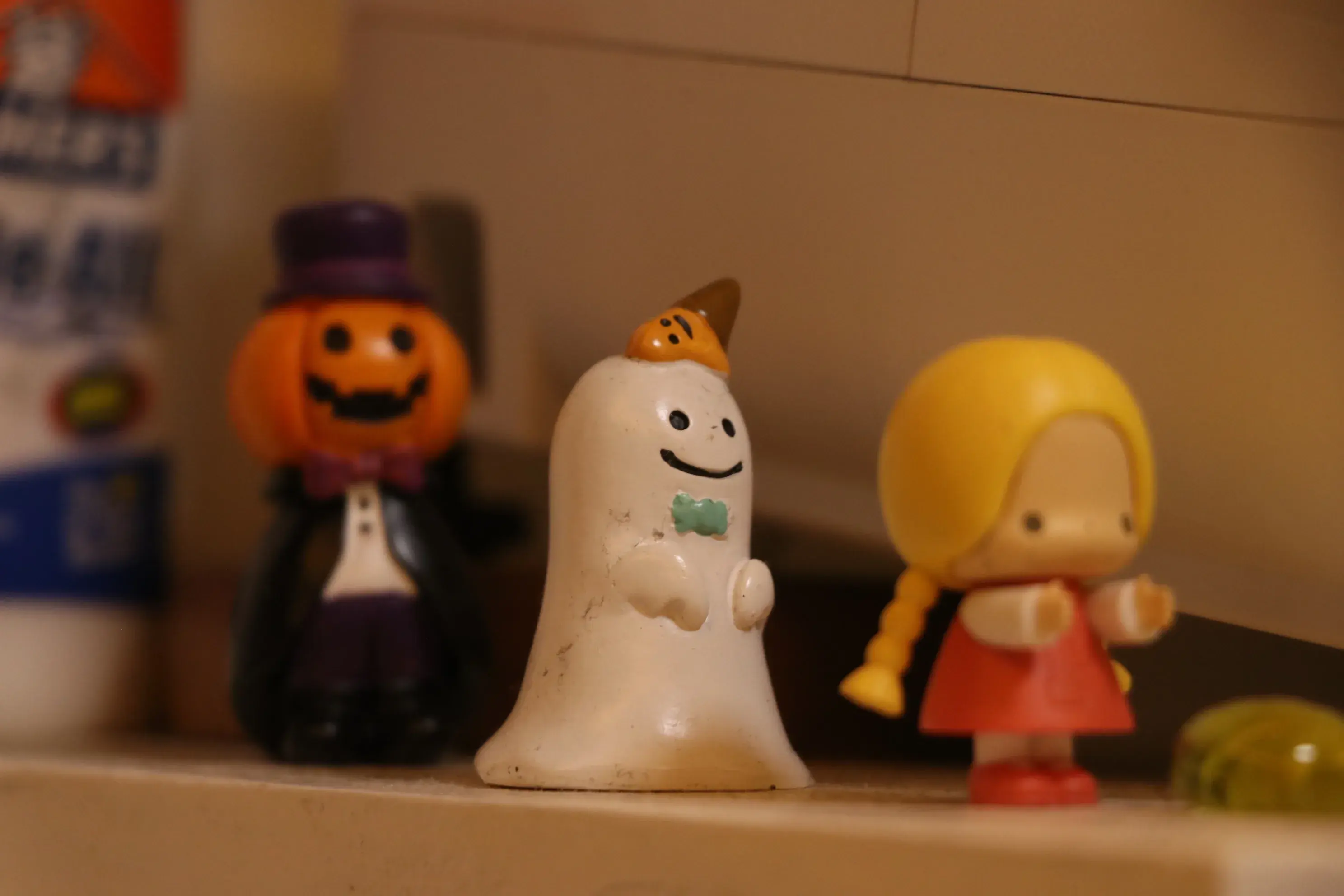 Small figurines on a shelf, including a smiling ghost, a pumpkin in a top hat, and a girl in a red dress
