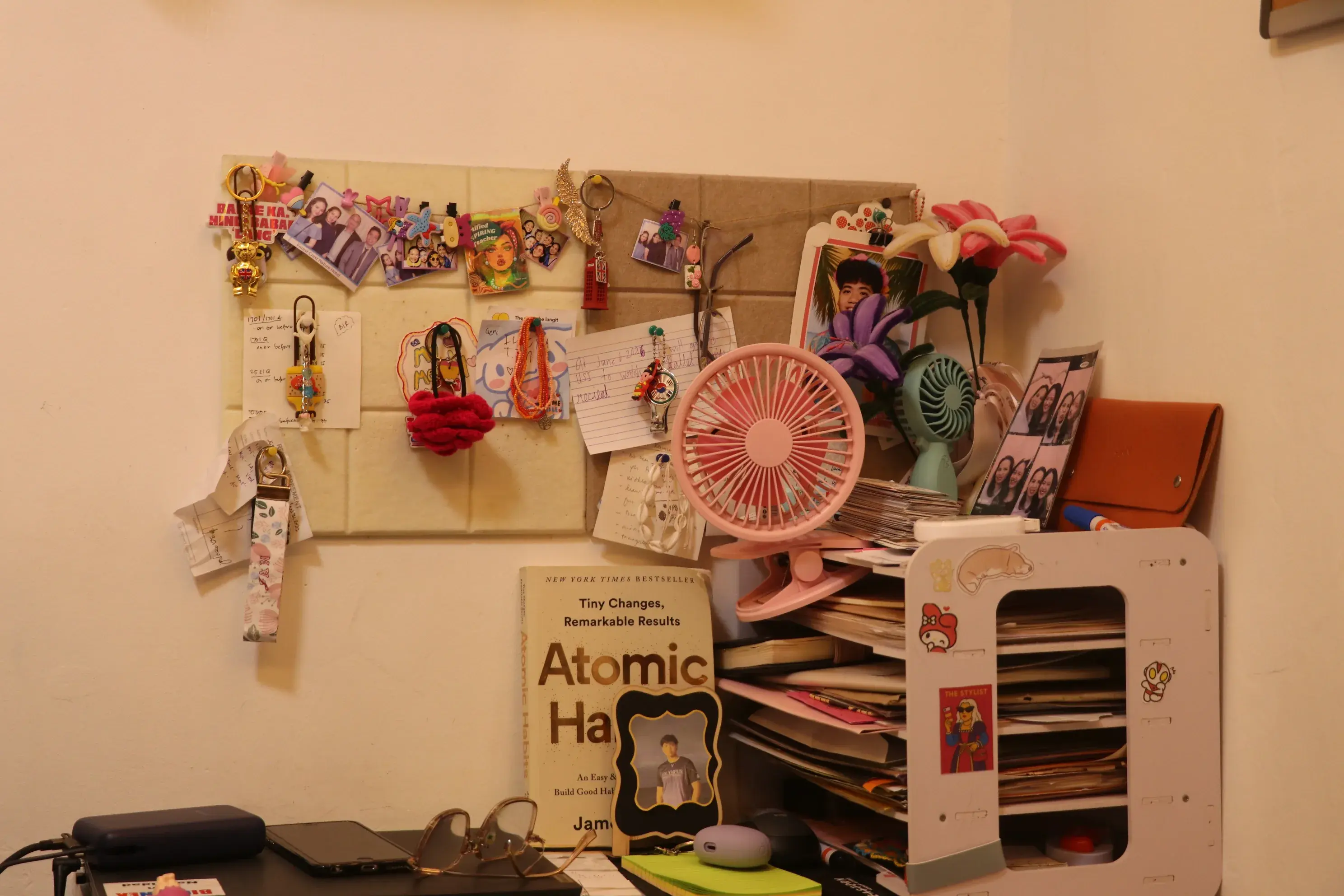 A desk corner with photos, notes, a small fan, and a stack of papers