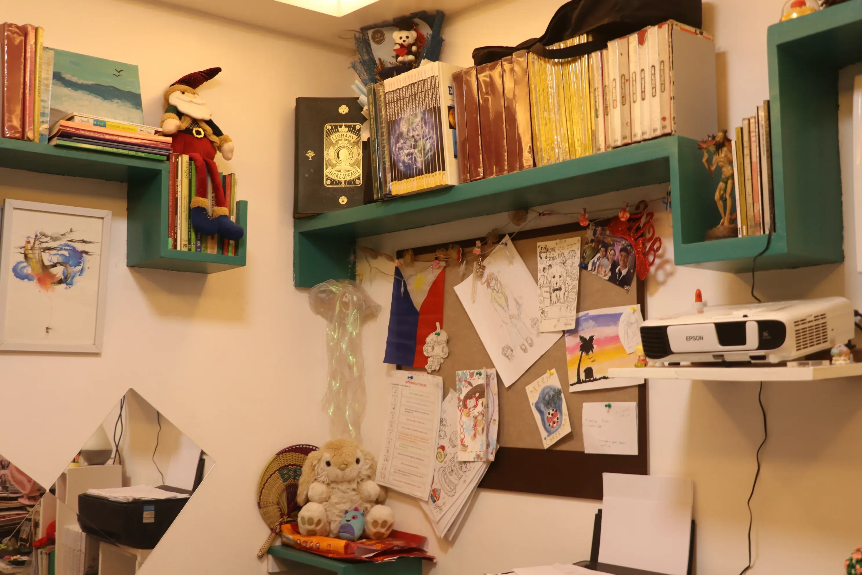Teal wall shelves with books, student art, a Philippine flag, and a projector