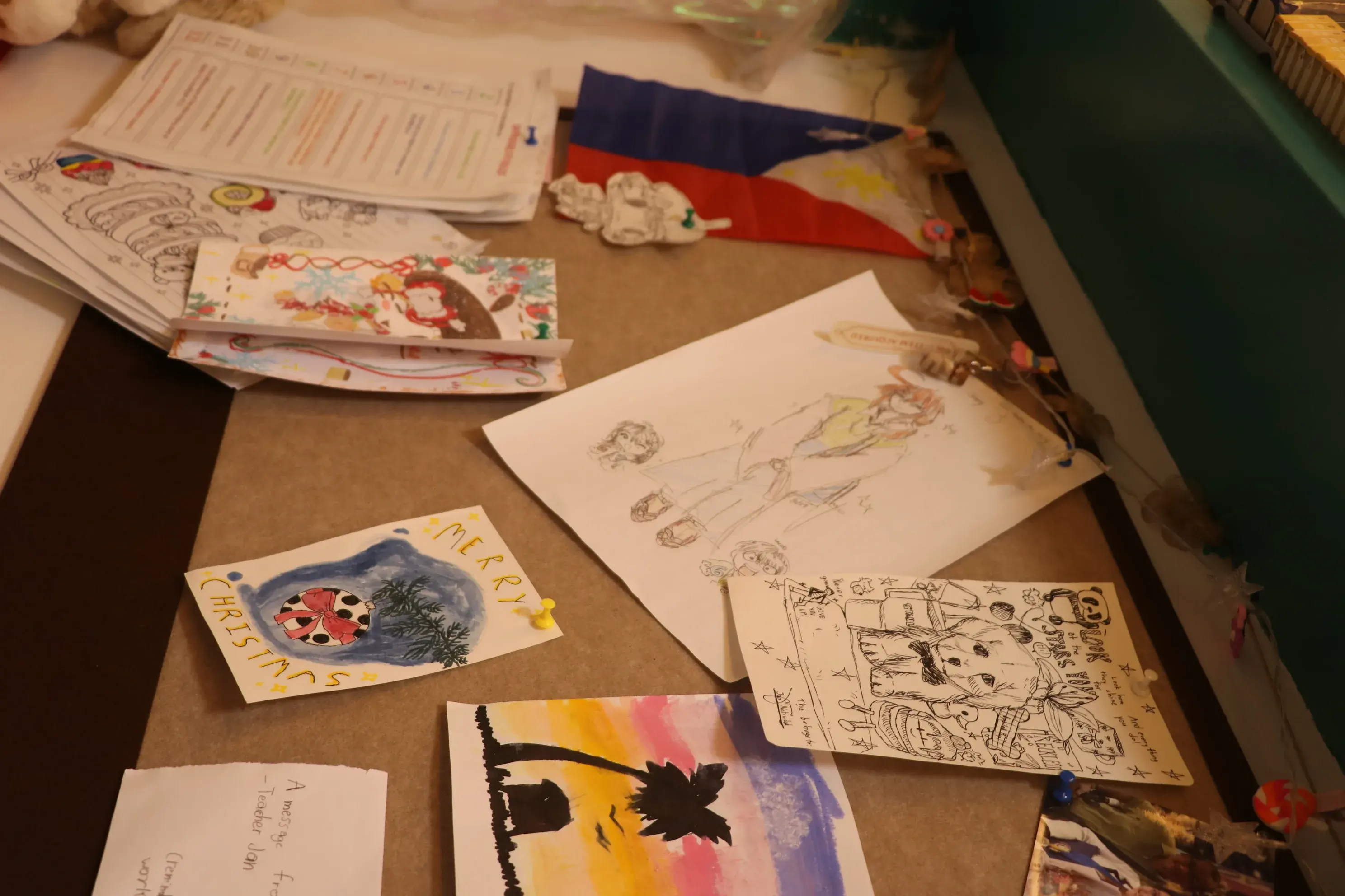 A corkboard of student drawings, cards, and a small Philippine flag
